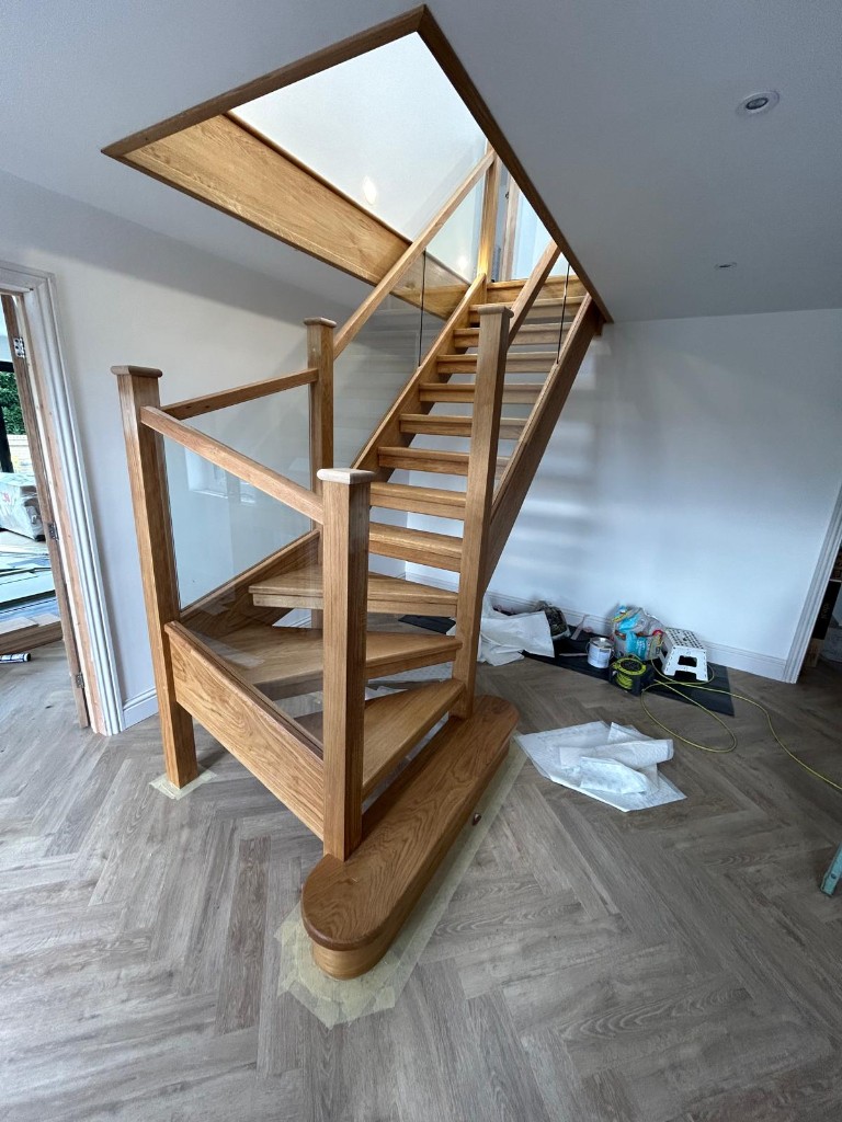 Side view of a custom solid oak open plan staircase with glass balustrading and a bullnose bottom step in Cliffe Woods, Kent